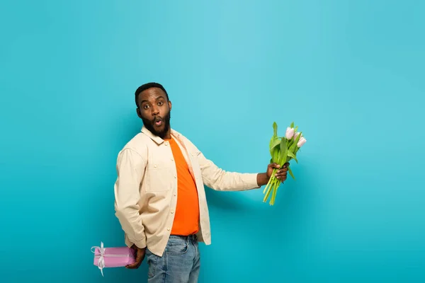 Surprised African American Man Holding Fresh Tulips Gift Box Blue — Stock Photo, Image