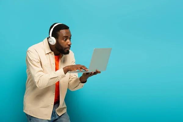 Surprised African American Man Headphones Using Laptop Blue Background — Stock Photo, Image