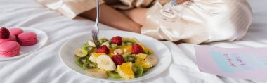 Meyve salatasının, badem kurabiyelerinin ve doğum günü tebrik kartının yanında oturan kadın manzarası. 