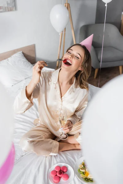 Весела Жінка Вечірній Кепці Тримає Келих Шампанського Біля Фруктового Салату — стокове фото