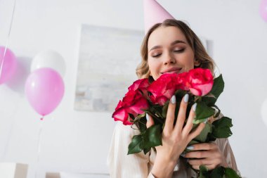 Parti şapkalı gülümseyen kadın doğum günü partisinde elinde güllerle 