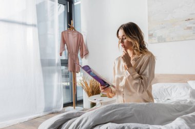 Genç bir kadın sabahları yatakta dergi okuyor. 