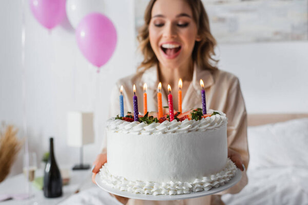 Birthday cake in hands of excited woman on blurred background in bedroom 
