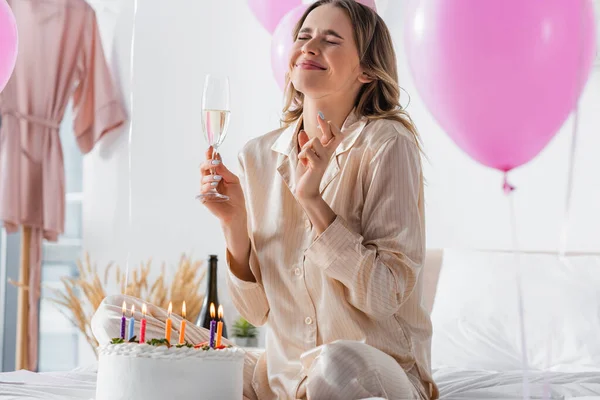 若いです女性でPajama保持シャンパンと交差指近く誕生日ケーキとともにキャンドル — ストック写真