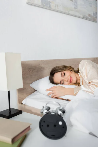 Smiling Woman Lying Bed Blurred Books Alarm Clock — Stock Photo, Image