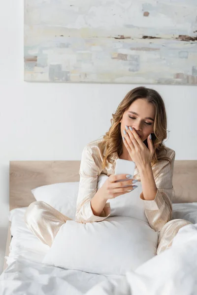 Kvinnan Gäspar Och Använder Smartphone Sängen — Stockfoto