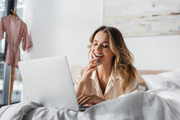 Smiling woman using laptop on bed in morning 