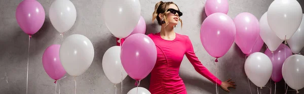 戴着太阳镜的时髦女人站在气球和灰色墙壁旁边 高举横幅 — 图库照片