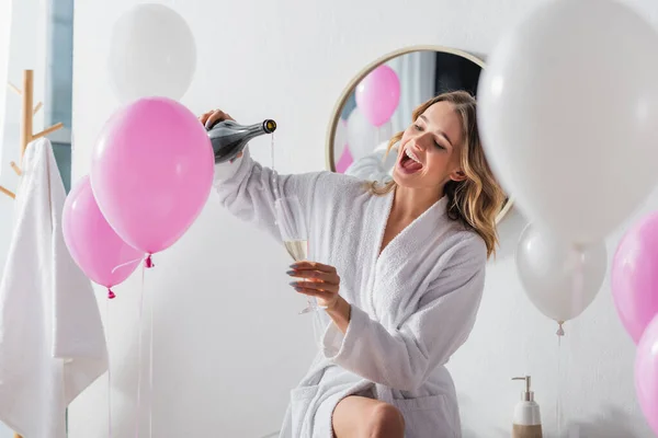 Fröhliche Frau Bademantel Gießt Champagner Neben Luftballons Badezimmer — Stockfoto