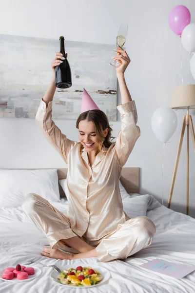 Positive Frau Mit Champagner Neben Grußkarte Makronen Und Luftballons Schlafzimmer — Stockfoto