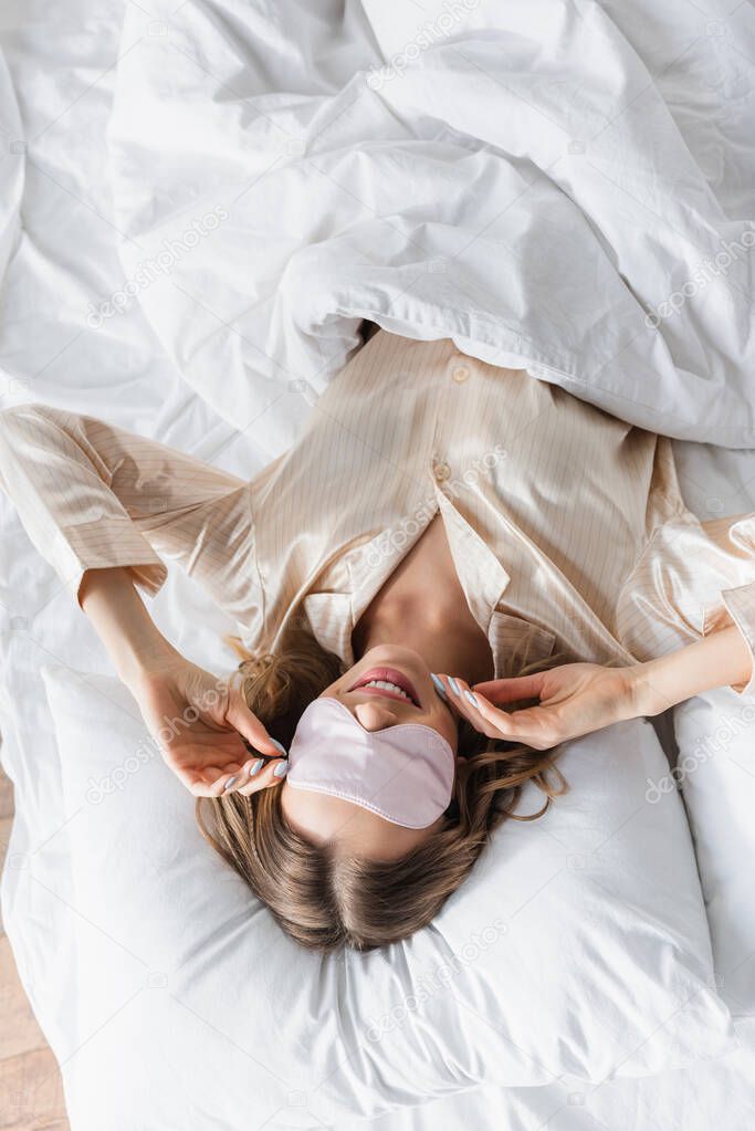 Top view of smiling woman in sleeping mask lying on bed 