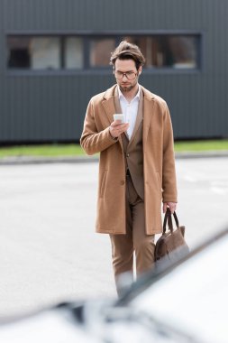 man in glasses and beige coat using mobile phone outside 