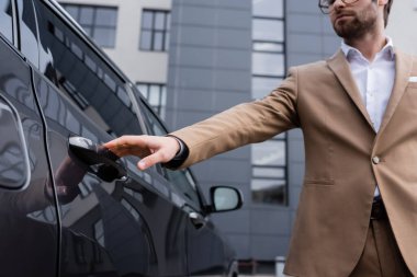 cropped view of man in beige jacket and glasses reaching car door