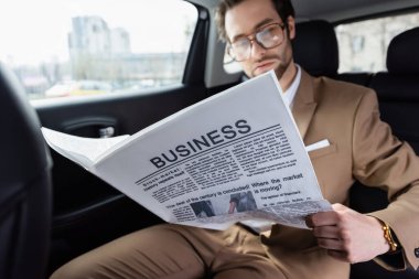 blurred man in glasses reading business newspaper in car 