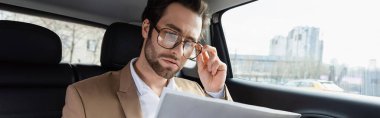 confident man adjusting glasses and reading business newspaper in car, banner