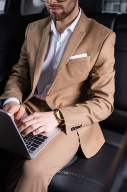 cropped view of businessman typing on laptop in car