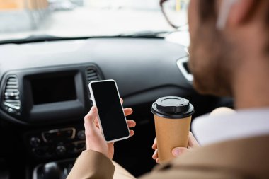 cropped view of blurred man in glasses holding smartphone with blank screen and paper cup in car 