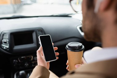 cropped view of blurred man in glasses holding smartphone with blank screen and paper cup in car  clipart