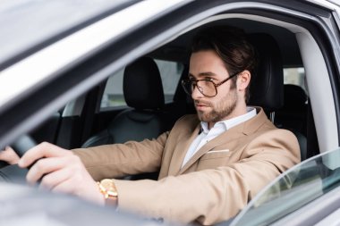 bearded man in glasses driving modern car 