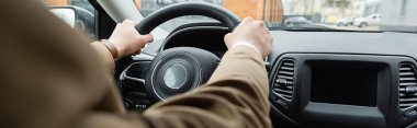 partial view of man in beige jacket driving car, banner
