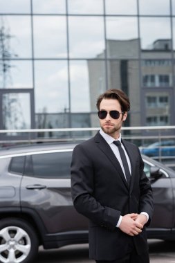 bearded safeguard in suit and sunglasses near car 
