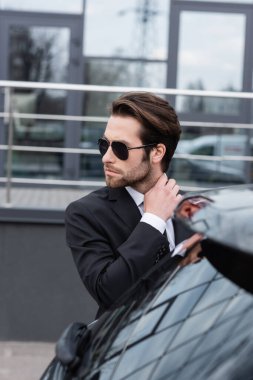 bearded man in suit and sunglasses near modern car 