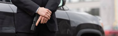 cropped view of bodyguard in suit holding gun near modern auto, banner