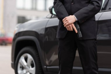 cropped view of bodyguard in suit holding gun near blurred modern auto