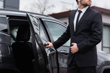 partial view of bearded bodyguard with security earpiece opening car door 