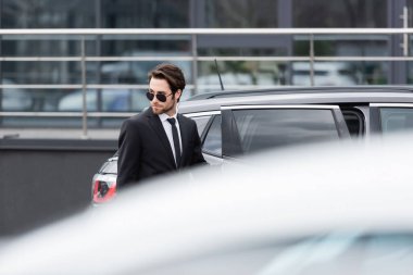 bearded businessman in suit and sunglasses on parking 