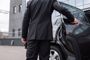 back view of bodyguard in suit holding gun and opening car door 
