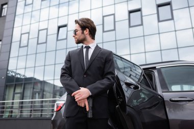 low angle view of bearded bodyguard in suit holding gun near car