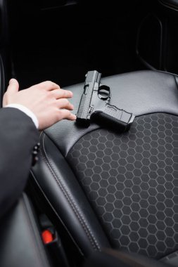 cropped view of bodyguard reaching gun on seat of modern automobile 