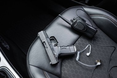 top view of walkie talkie, black gun and security earpiece on car seat 
