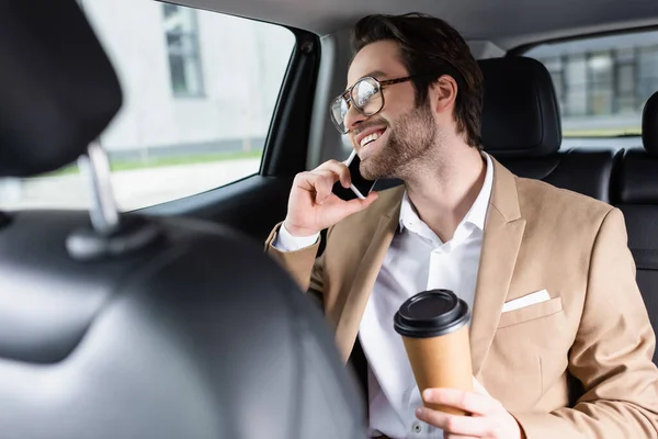 Hombre Alegre Traje Gafas Sosteniendo Taza Papel Hablando Teléfono Inteligente —  Fotos de Stock