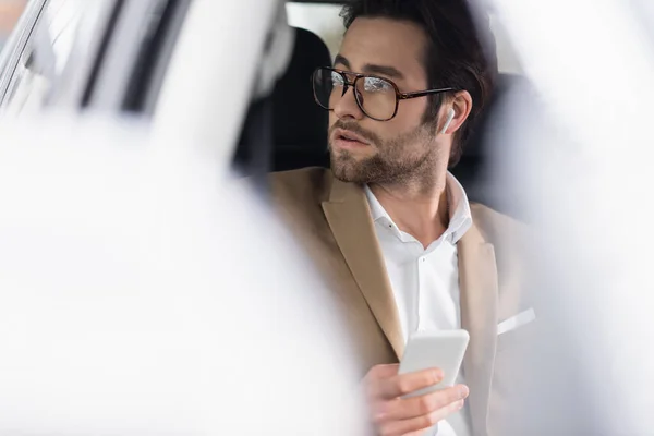 Geschäftsmann Mit Brille Und Drahtlosen Kopfhörern Hält Smartphone Auto — Stockfoto