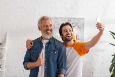 Oğlu akıllı telefondan selfie çekerken adam jest yapıyor. 