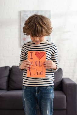 Boy looking at gift card with i love you dad lettering at home  clipart