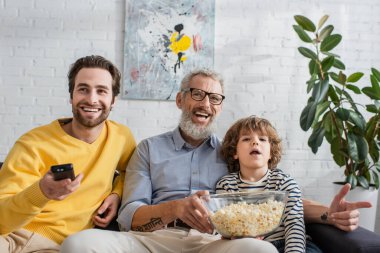 Gülümseyen adam ve çocuk evde patlamış mısırla televizyon seyrediyor. 