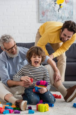 Neşeli ebeveynler halıdaki çocukla yapı taşı oynuyorlar. 