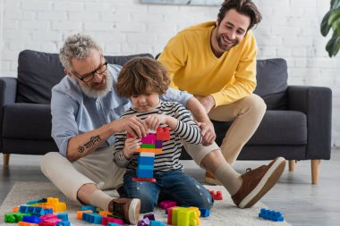 Çocuk oturma odasında büyükbaba ve babasının yanında yapı taşı istifliyor. 