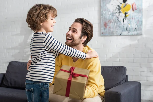 Enfant Joyeux Embrassant Père Avec Présent Sur Premier Plan Flou — Photo