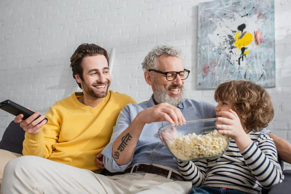 Usmívající Muž Dálkovým Ovladačem Sedí Poblíž Otce Syna Popcornem Gauči — Stock fotografie