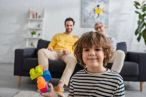 Jongen Met Bouwstenen Zoek Naar Camera Buurt Van Ouders Wazige — Stockfoto