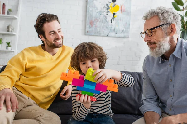 Menino Jogando Blocos Construção Perto Avô Sorrindo Pai Sofá — Fotografia de Stock