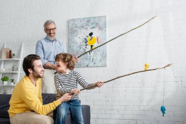 Baba ve neşeli oğul oyuncak avcılığı oynuyorlar. Bulanık büyükbabanın yanında. 