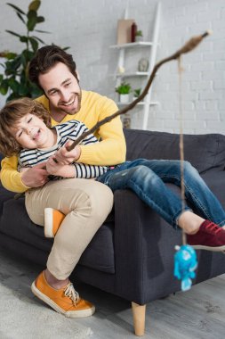 Positive father and son playing toy fishing at home clipart