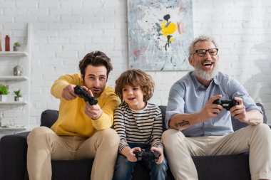 KYIV, UKRAINE - 12 Nisan 2021: Gülümseyen çocuk baba ve büyükbabasıyla video oyunu oynuyor 