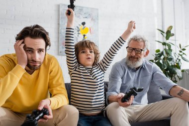 KYIV, UKRAINE - 12 Nisan 2021: Çocuk üzgün ebeveynlerin yanında joystickle evet işareti yapıyor 