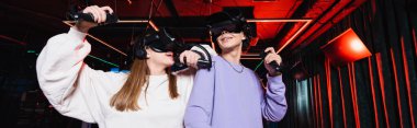 Kulaklık takmış mutlu genç oyuncular VR oyun sahasında eğleniyorlar, afiş